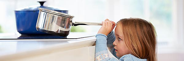 Little girl lifting saucepan off stove